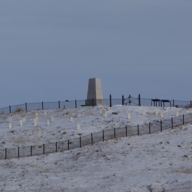 Photograph of hill with monument and headstones with snow on the ground