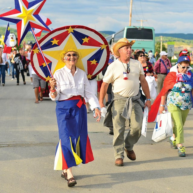People walking in a parade holding Maine Acadian flags