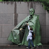 A child reaches up to touch a large bronze statue of Franklin Roosevelt.
