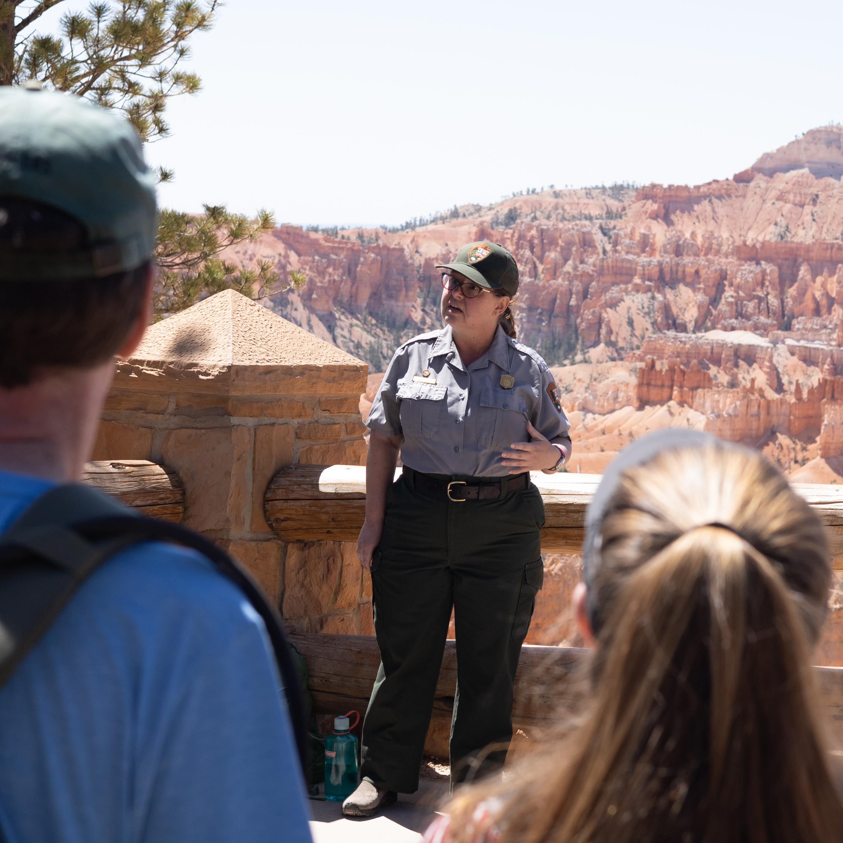A ranger in uniform stands in front of a crowd with a background of red rock formations