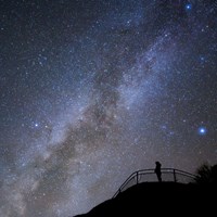The black silhouette of a person standing at a viewpoint with the milky way in the backgroundn