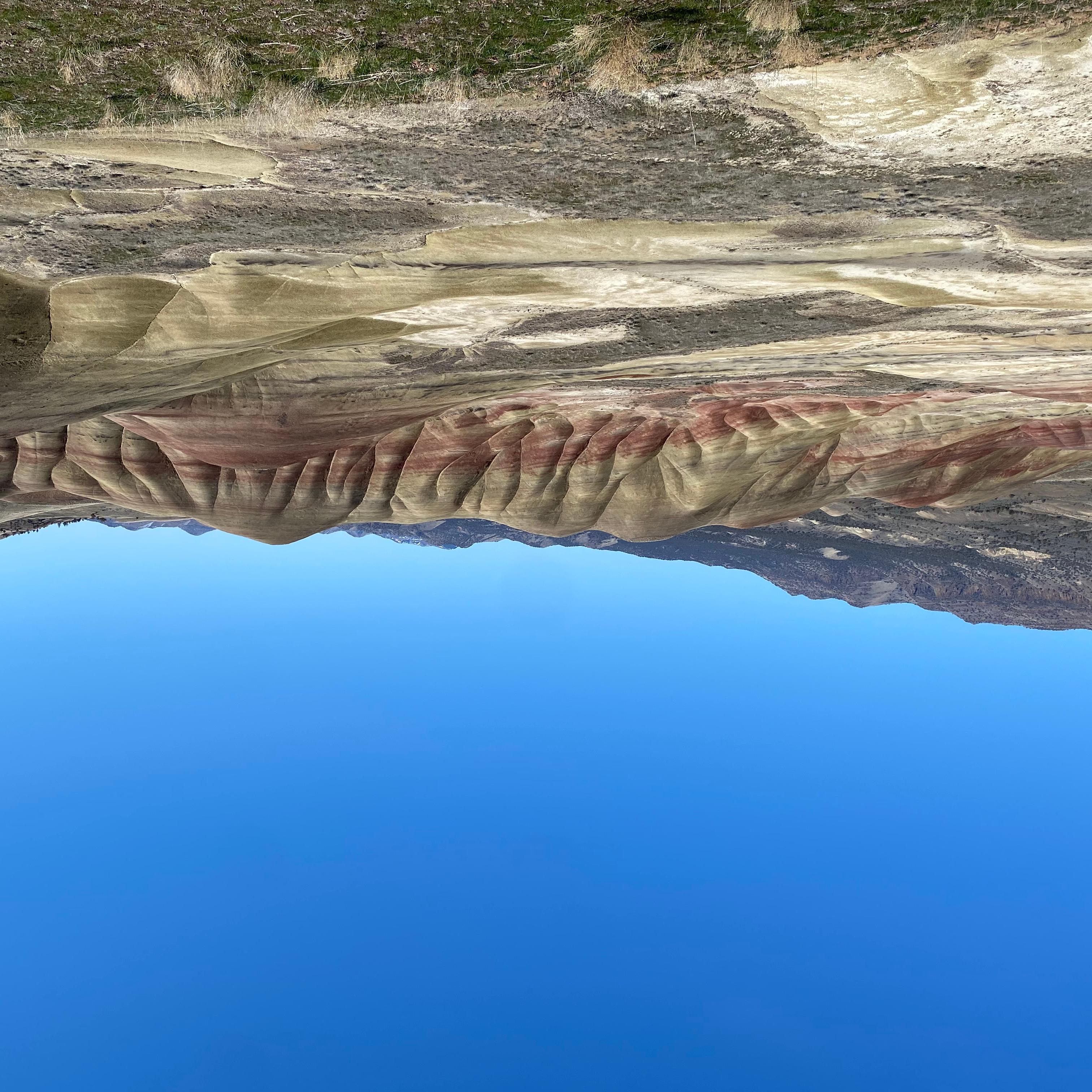 Red and yellow striped hills with tan grasses in the foreground and blue skies.