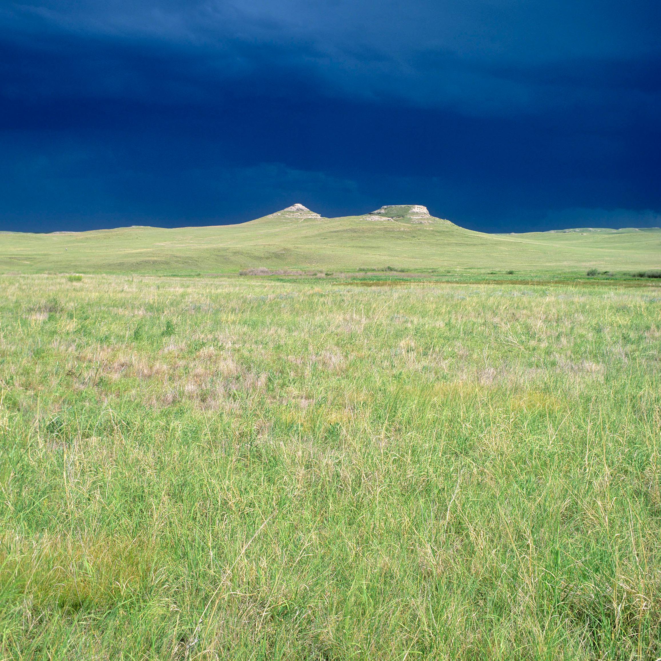 The sun illuminates the fossil hills with a dark, stormy sky in the background.