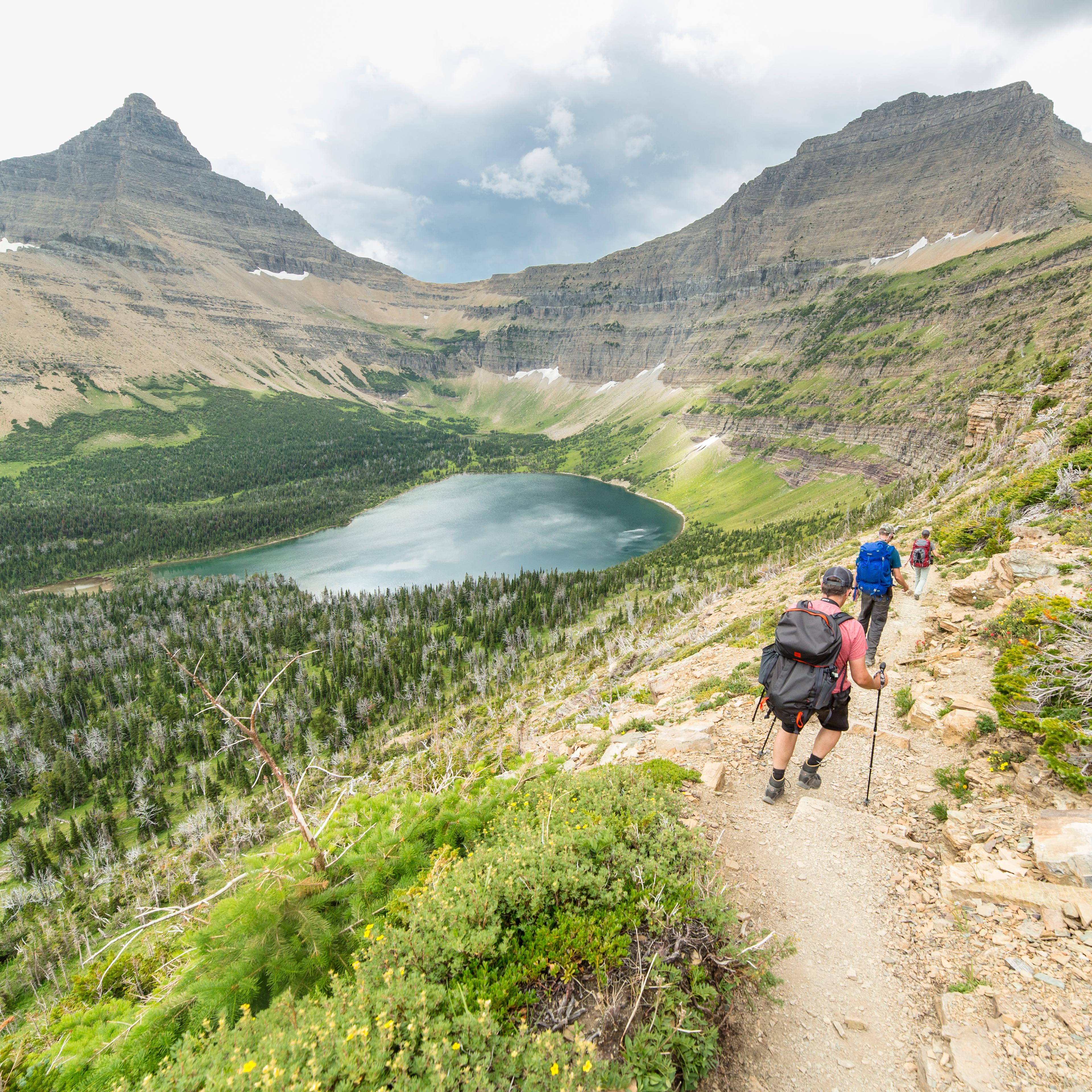 hikers on a trail near a clear blue lake