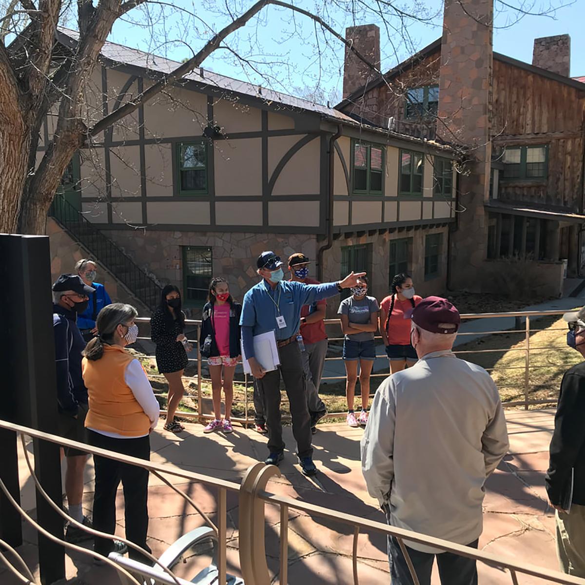 A person in a blue shirt points out a building to a group of people. 