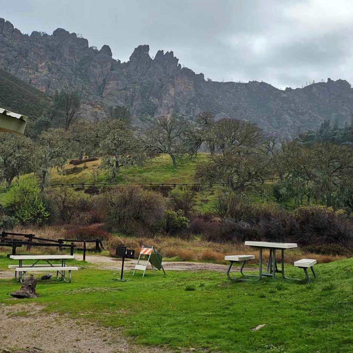 Shade structure and two picnic tables set before rock formations peering out of fog in winter