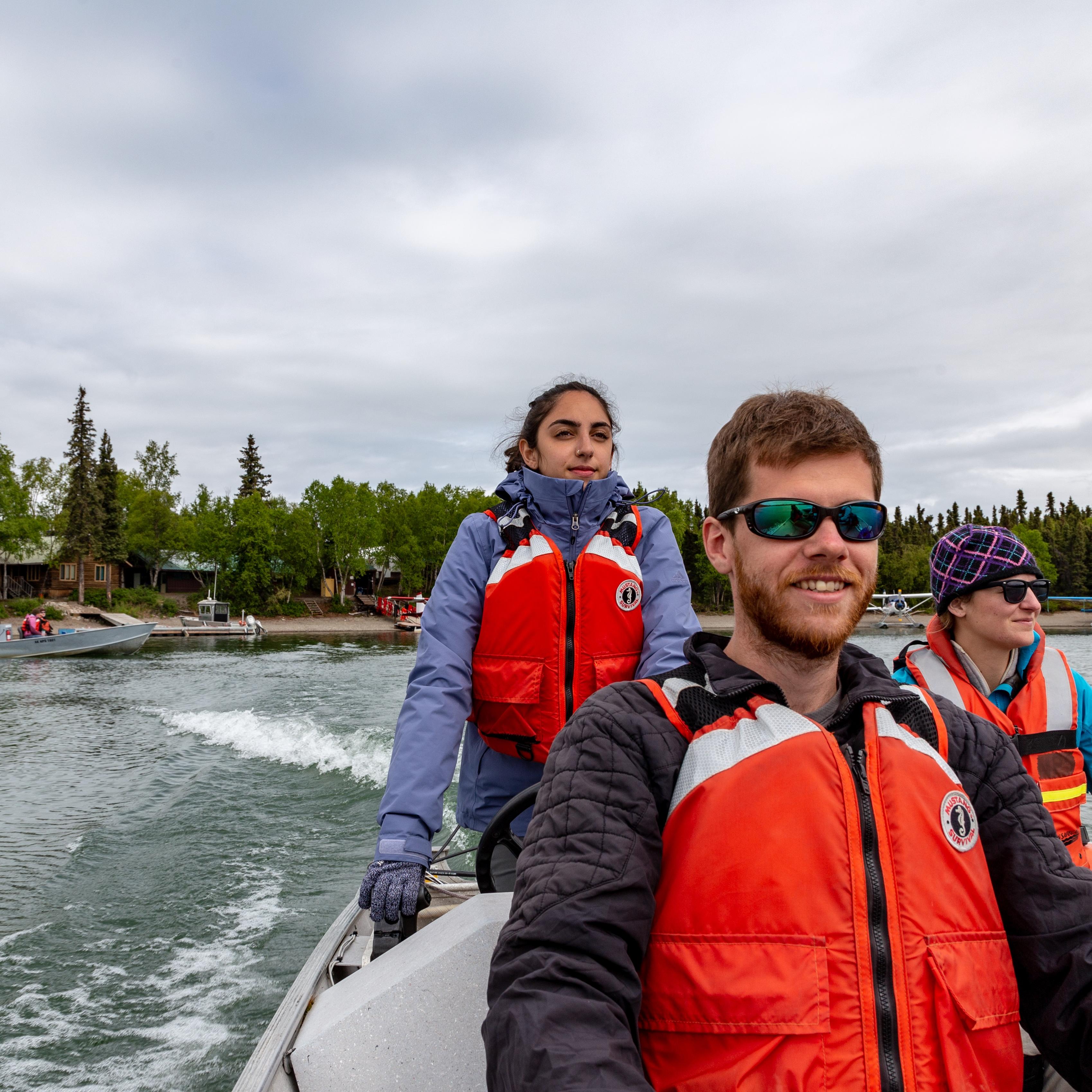 3 people wearing PFDs ride in a boat from the shore of Port Alsworth