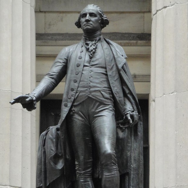 A metal, larger than life, statue of George Washington; his right arm outstretched.