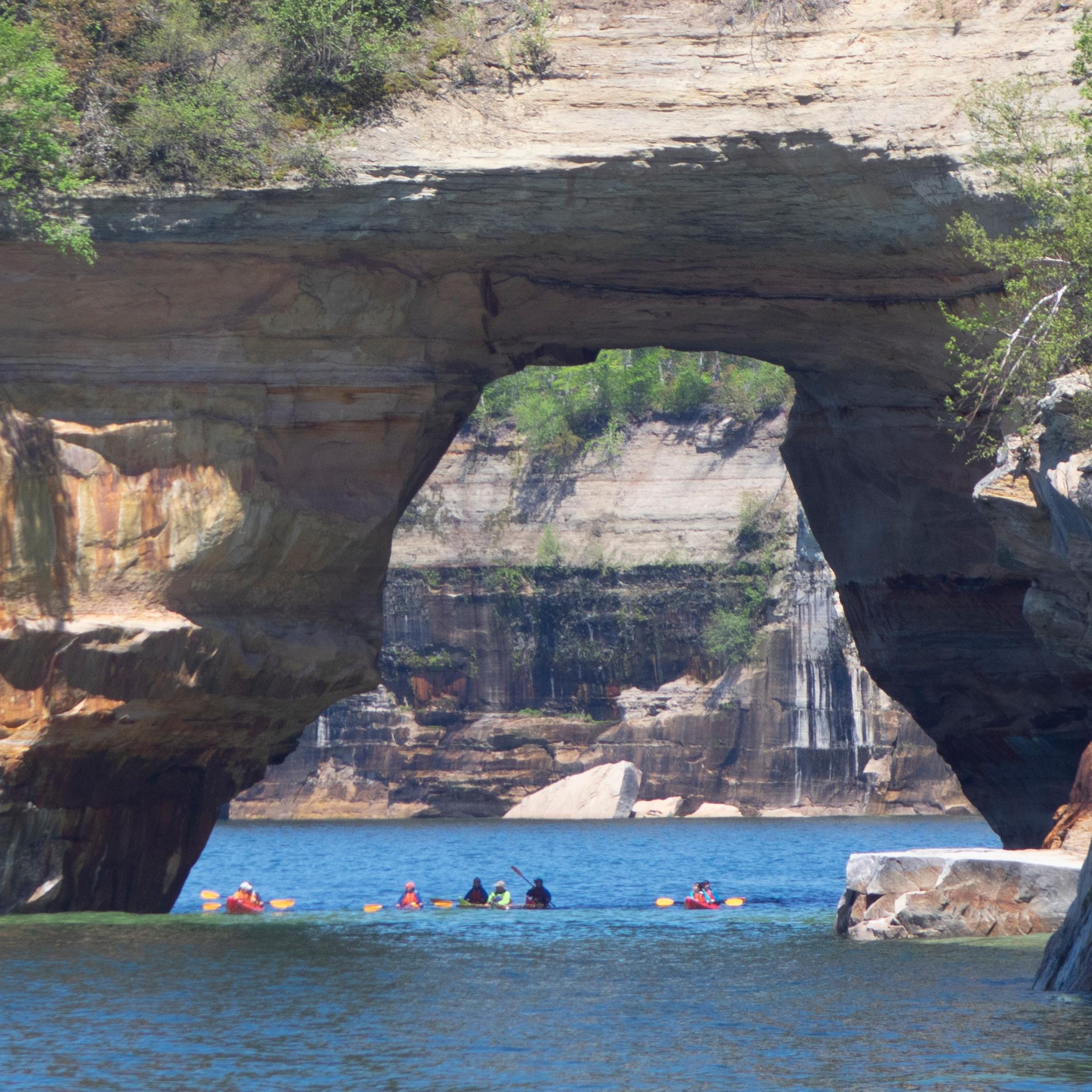 Group of kayakers under large sandstone arch