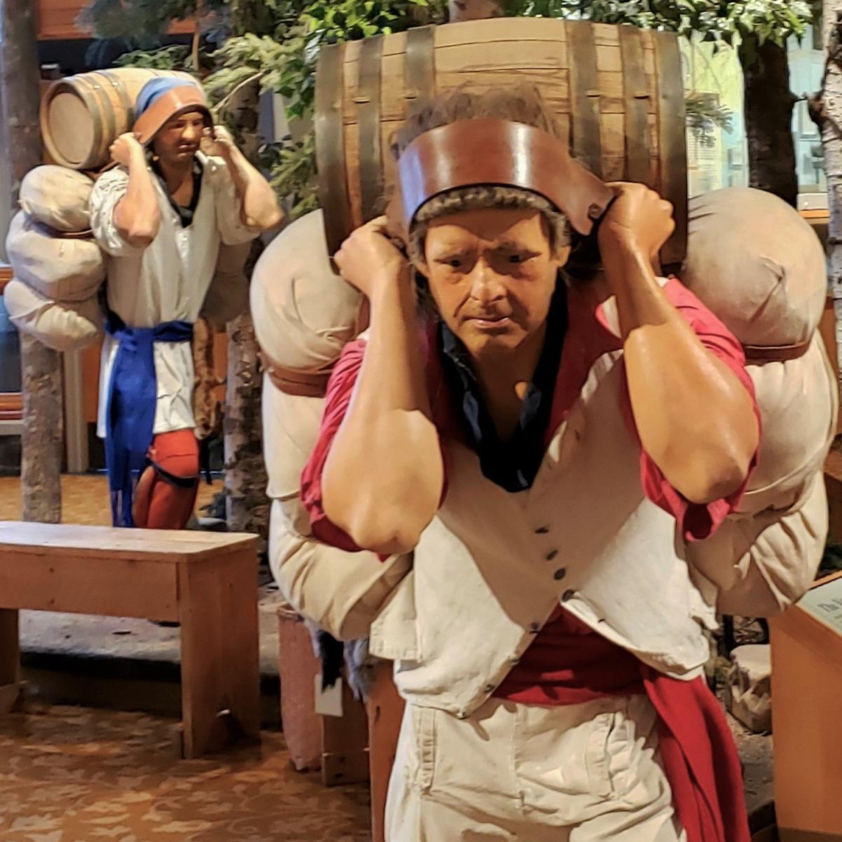 Mannequins dressed in historic clothing carrying heavy looking bales of trade goods.