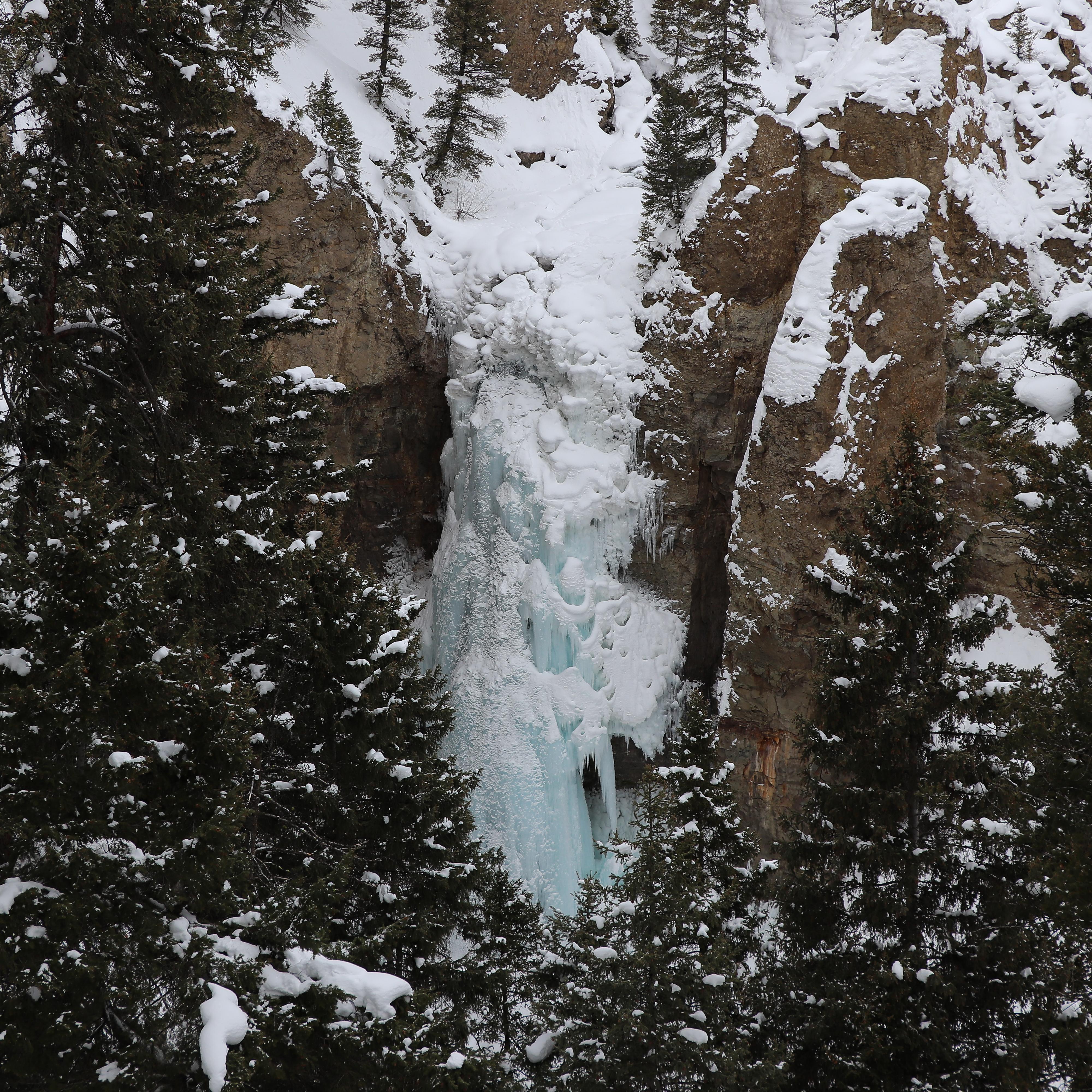 Icicle formations encase a waterfall surrounded by columns of rock.