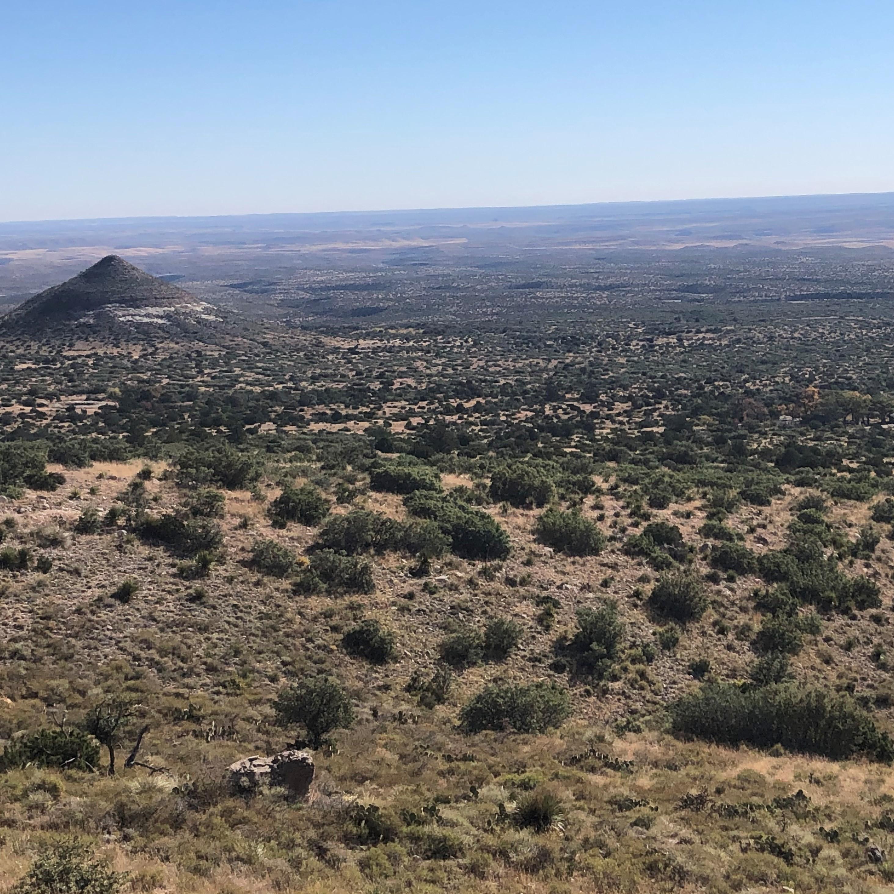 A desert mountain landscape with buildings and a prominent point in the background. 