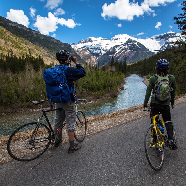Two bicyclists view mountains from a road along a river