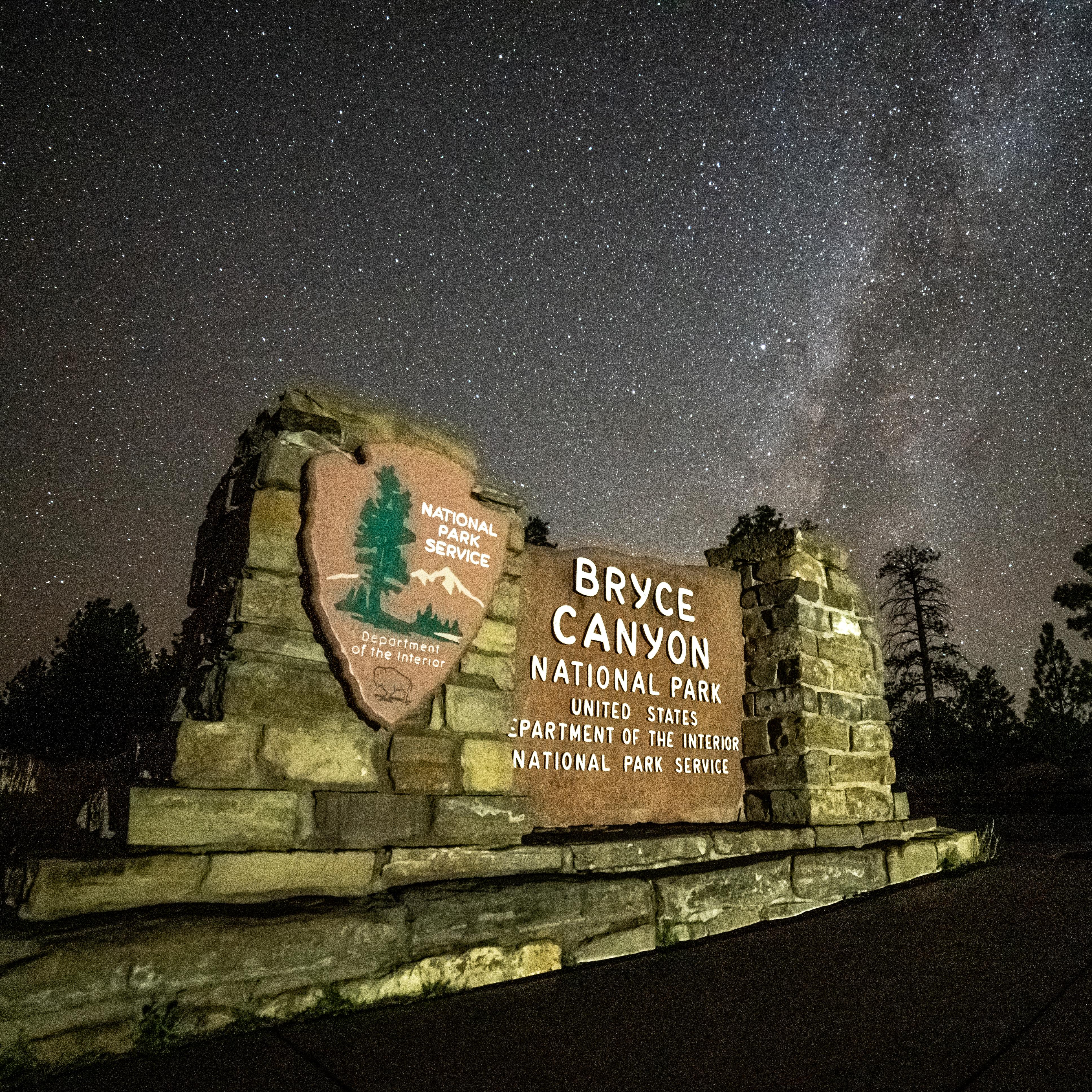 An illuminated Bryce Canyon park entrance sign against a backdrop of stars in a dark sky