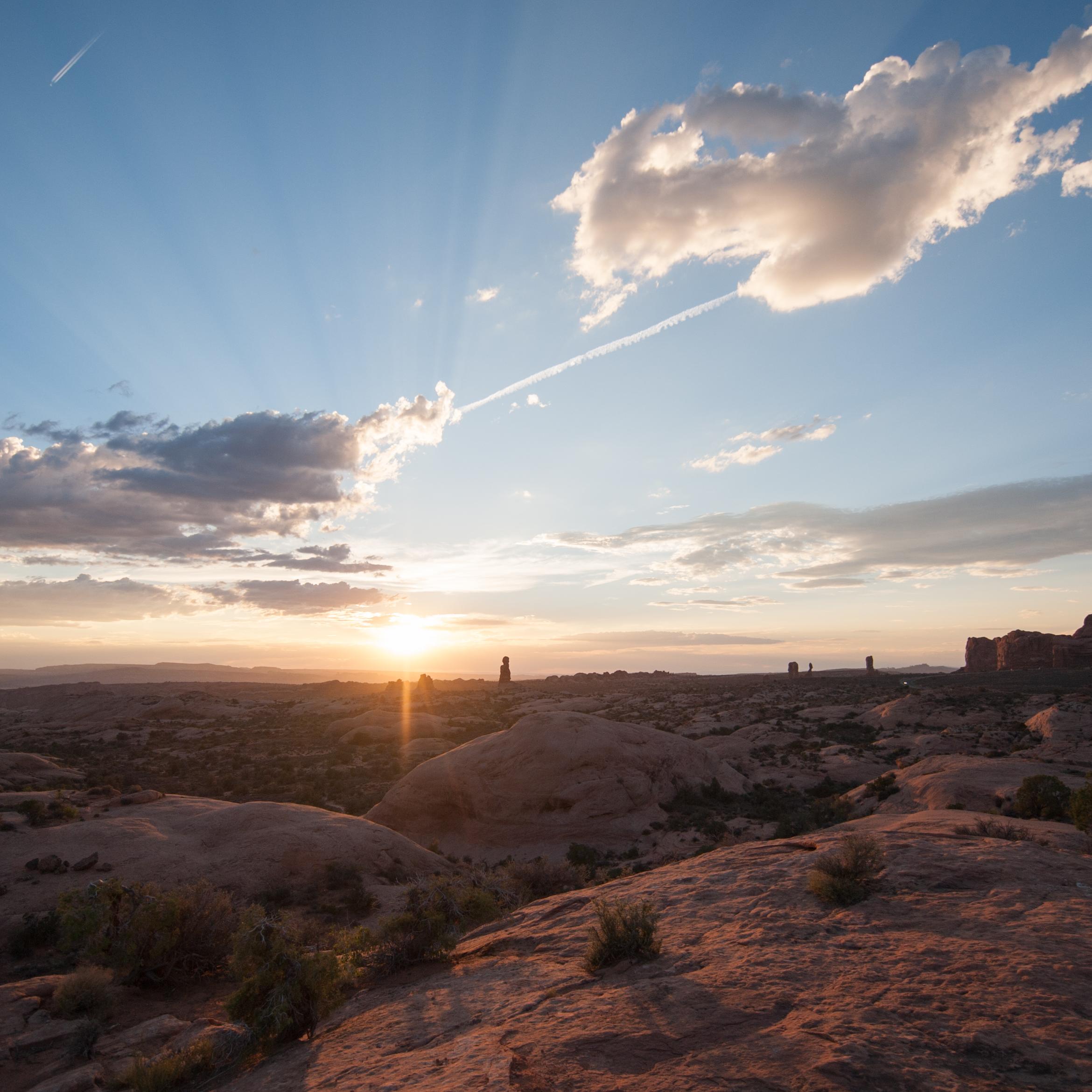 the sun sets behind a rocky landscape with clouds overhead