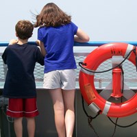 two youth looking at open water from deck of a large boat