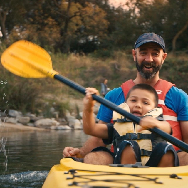 Father and son joyfully paddle a canoe down a wooded calm river