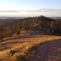 wide gravel path at sunrise on an open hillside with many forested hills in the distance