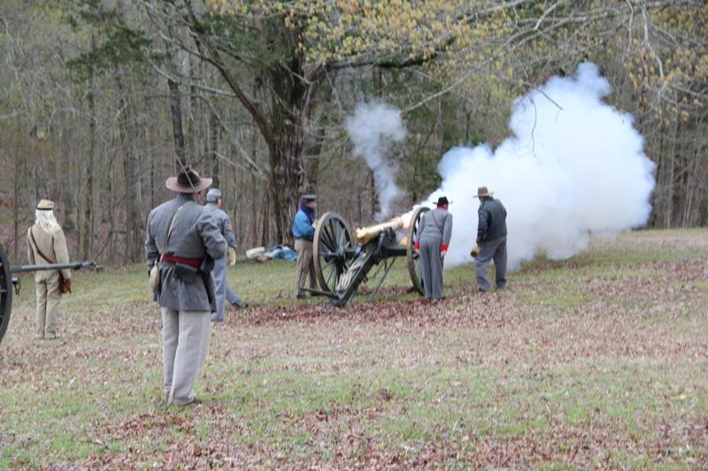 Living historians in period uniforms fire a bronze cannon.