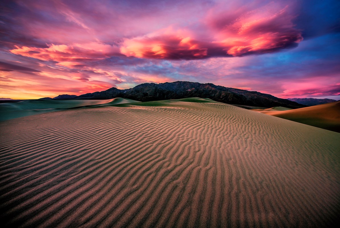 Pink clouds are lit up in the setting sun over Mesquite Flat Sand Dunes