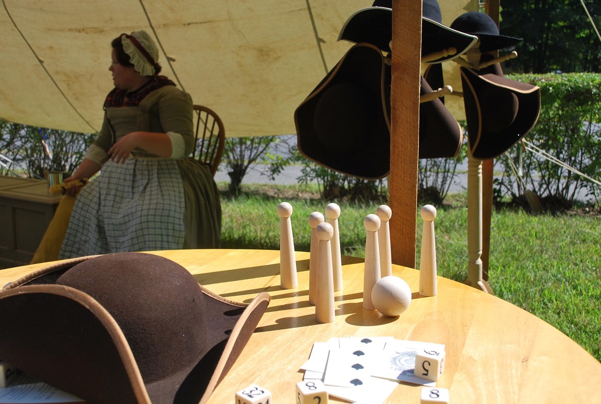 A colonial hat next to a set of tabletop skittles under a canvas awning