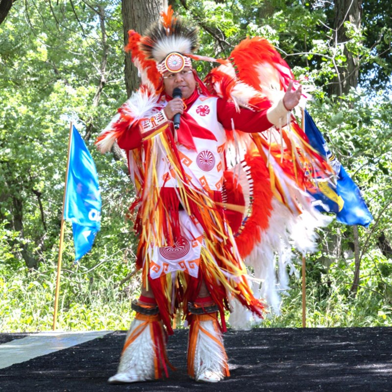 Man dressed in traditional Native American ceremonial dress speaks to audience.