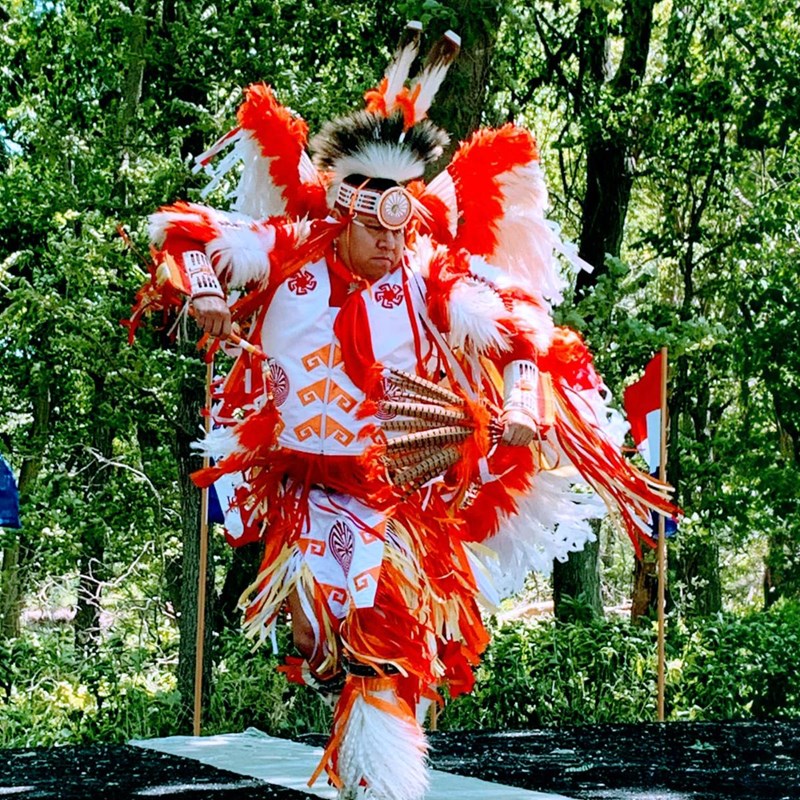 Man dressed in traditional Native American ceremonial clothing dances.