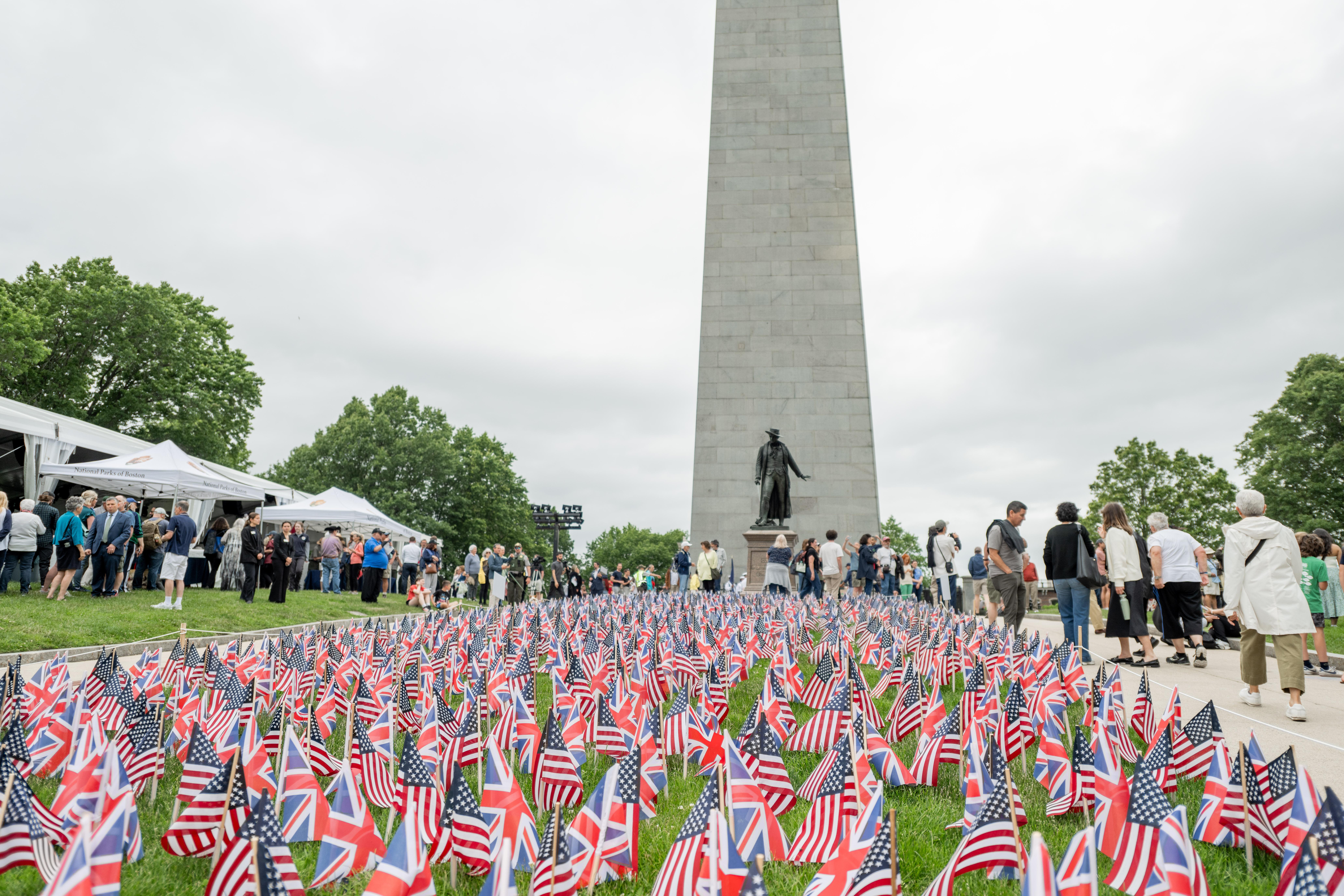 British and American flags planted on the grounds in front of the Bunker Hill Monument