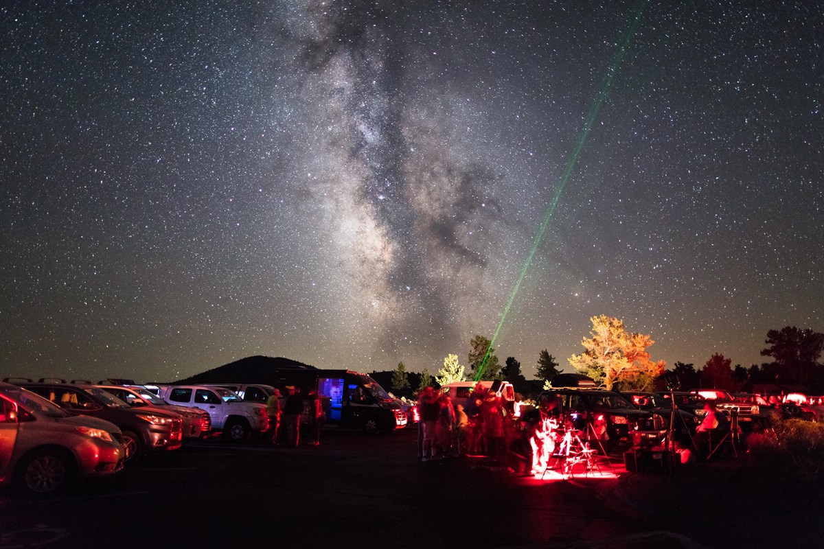 the milky way and many stars above people and telescopes as a ranger points with a green laser