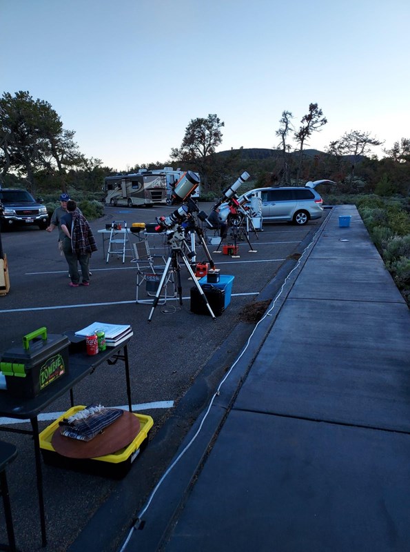 people setting up telescopes in a parking lot at sunset