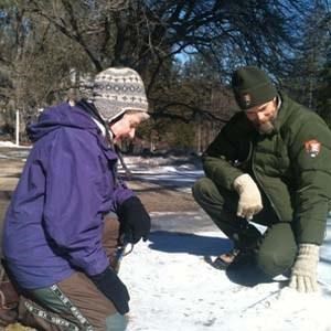 Visitor and ranger looking at animal tracks in the snow