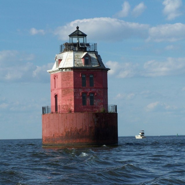 red lighthouse sitting up high in the water, Lighthouse is red six-sided house with mansard roof