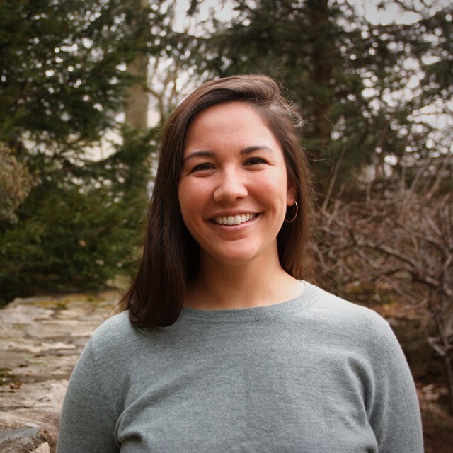 Smiling Asian woman with shoulder-length brown hair standing in the woods.