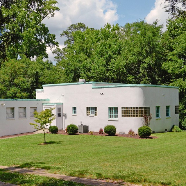 A white, flat-roofed house with a blue-green trim on the roof and windows