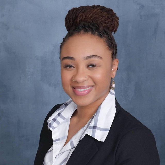 A Black woman wearing a blue and white shirt and a black suit jacket