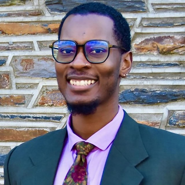 Black man wearing a purple shirt and a suit jacket.