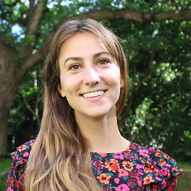 White woman with long brown hair wearing a floral dress.