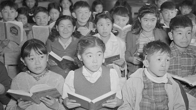 rows of children looking forward holding books, some smiling, some staring.