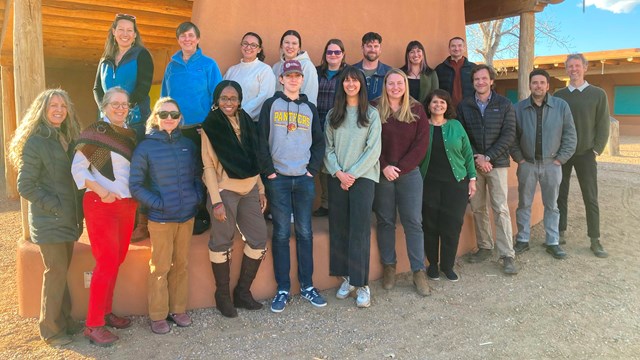 A group of people stand in front of an adobe building for a photo.