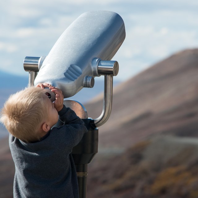 Small boy looking through binoculars into the sky. NPS/Lian Law