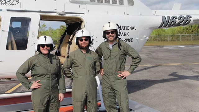 Three NPS employees in flight suits in front of a helicopter.