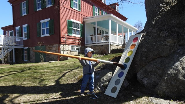 A child lifts an oversize paint brush