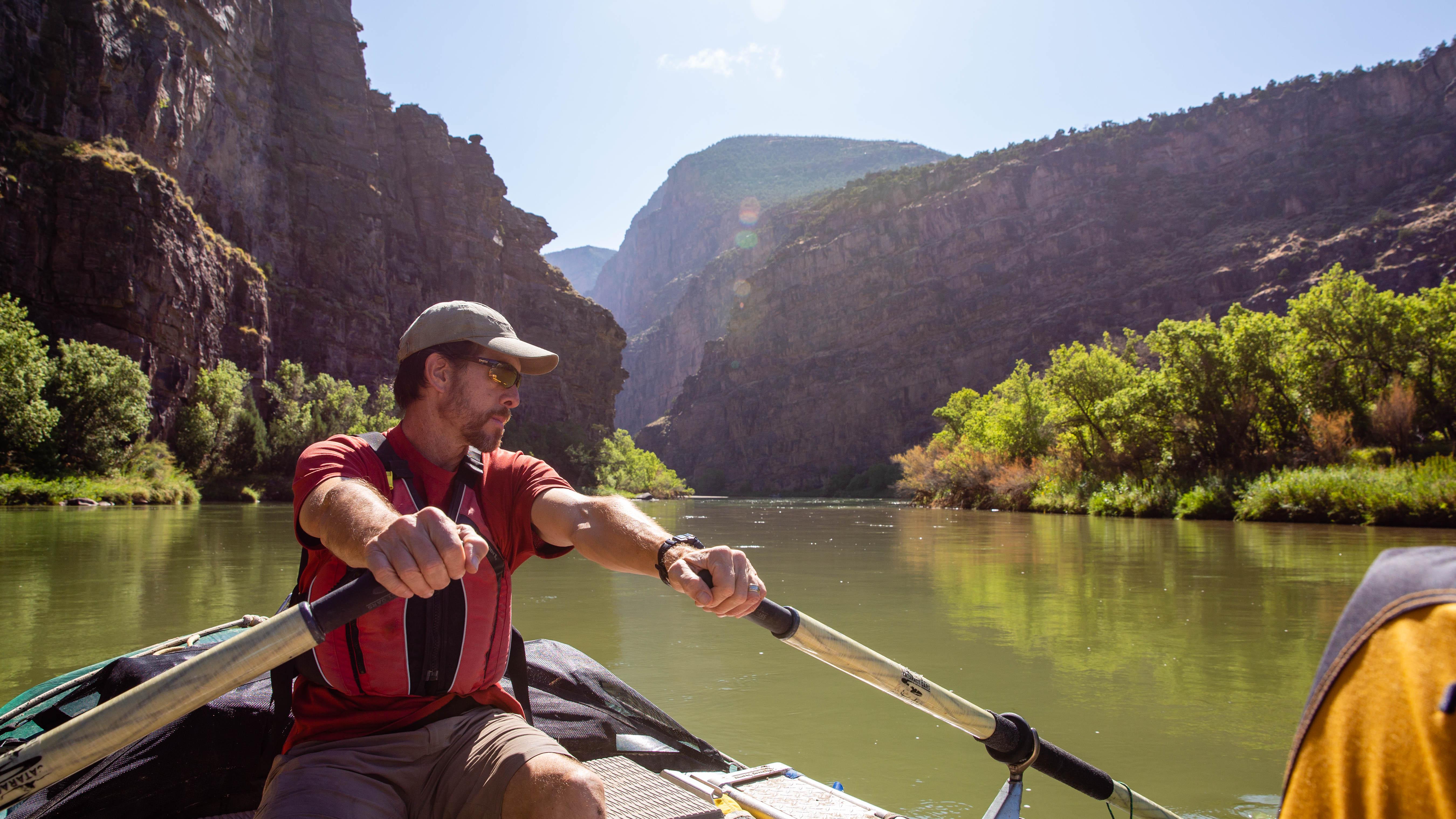A man rowing a raft down a canyon river, surrounded by towering rock walls