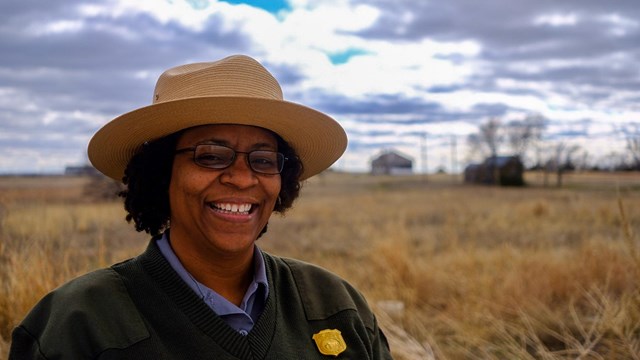 An African American woman in uniform standing in a prairie smiles at the camera. 