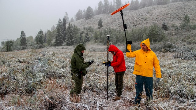 3 archeologists holding remote sensing and mapping equipment in a snowy field
