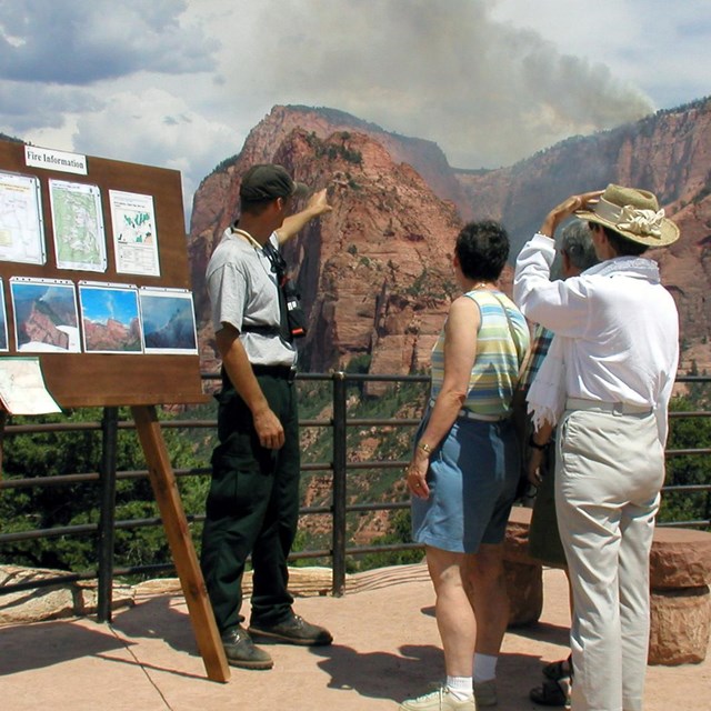 Ranger telling park visitors about fire safety with smoke in the distance