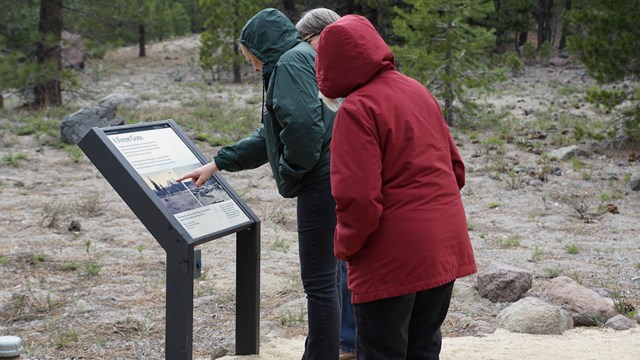 Two people view an angled exhibit along a trail. 