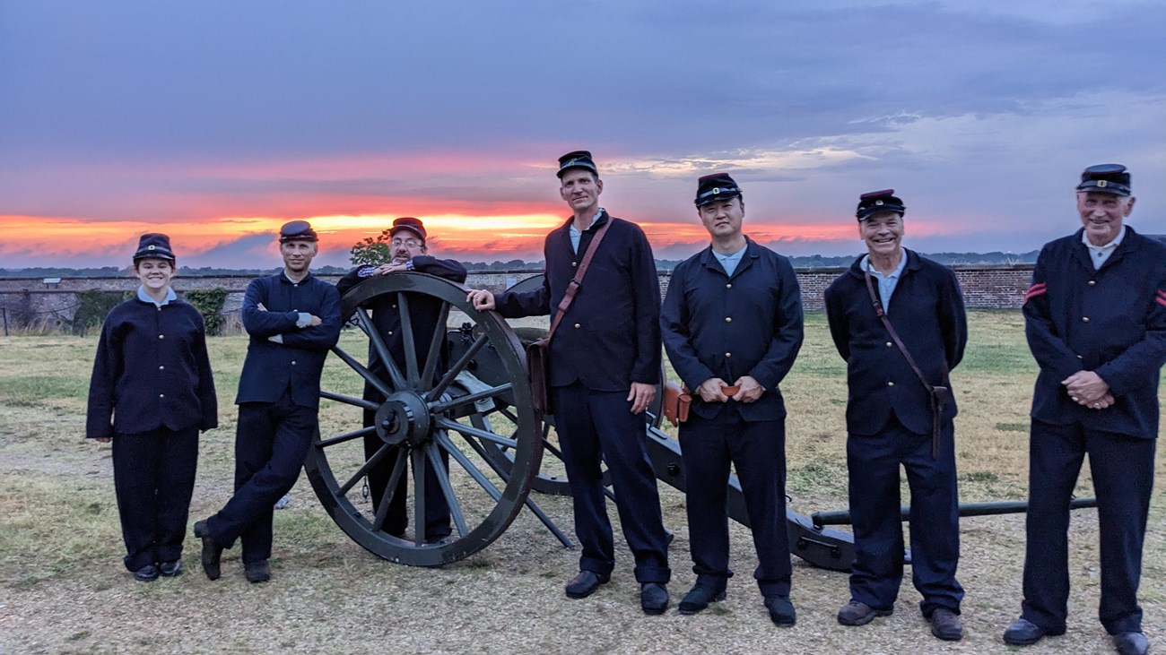 7 men and women in Union uniforms pose with a cannon