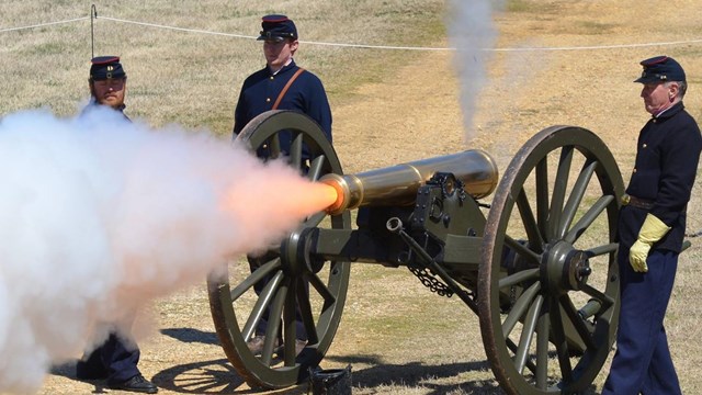 Three living historians around a field cannon that is firing smoke out of the barrel