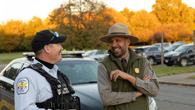 A park ranger and a police officer stand smiling next to each other.